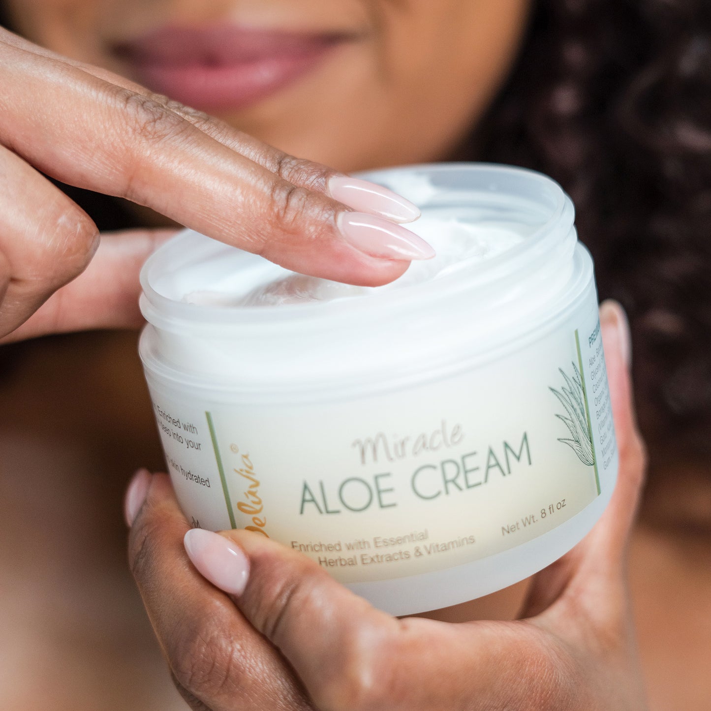 Smiling African American woman dipping her fingers in the Deluvia Miracle Aloe Cream 