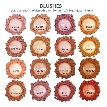 Photo of sample swatches of Demure loose mineral blush shades including hint of pink, satin rose, bloom, go bronze, natural radiance, peacy, mocha rose, mauve, pink fusion, sienna rose, spiced mocha, bold berry, sweet orange, sunrise, cinnamon, and brick.