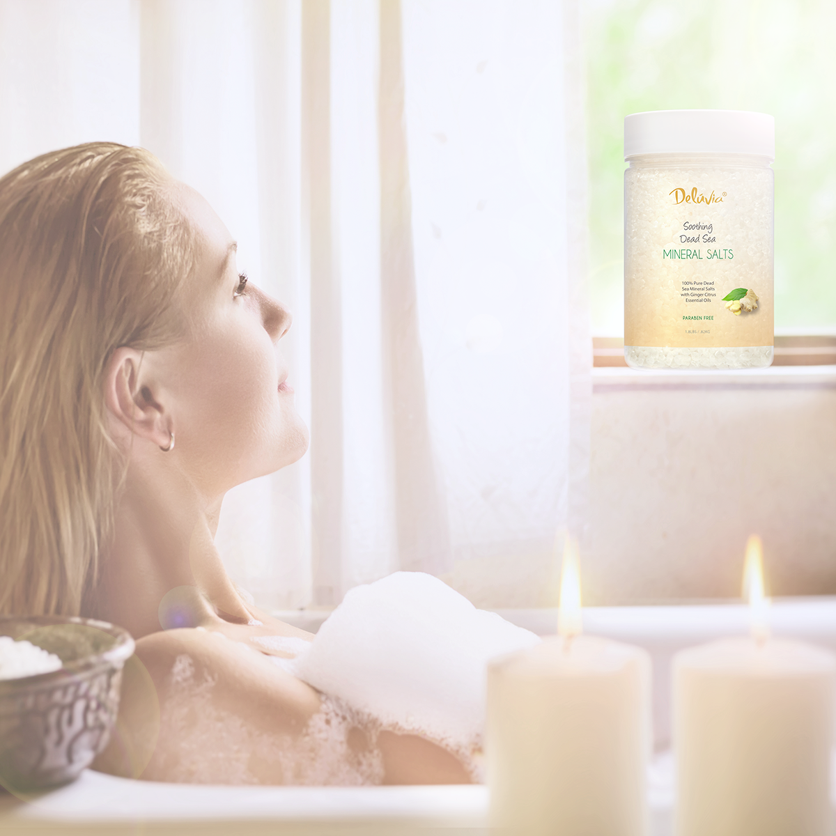 Photocomposition of 1.8 lbs jar of Deluvia Dead Sea Mineral Salts with a woman in a bathtub with foam looking at a window